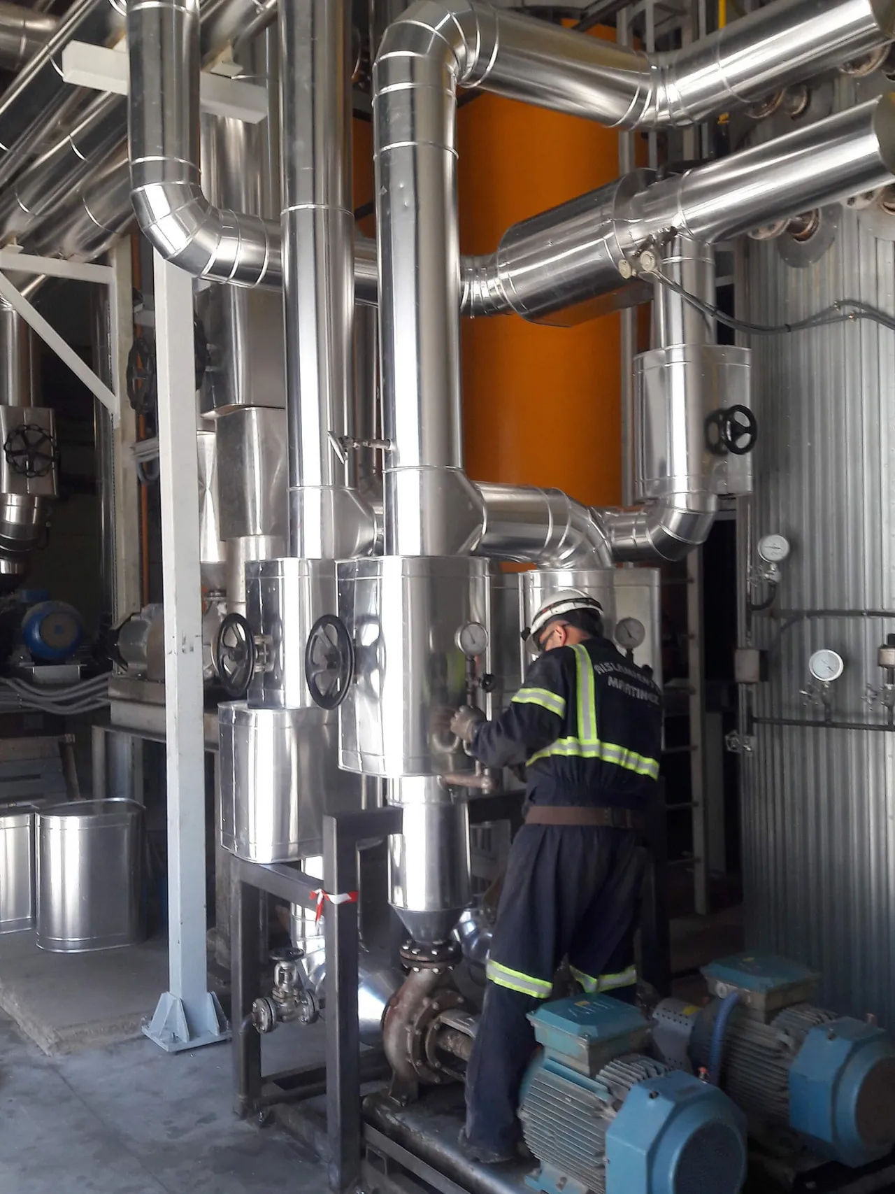 Operario trabajando entre tuberías y equipos de una instalación industrial.